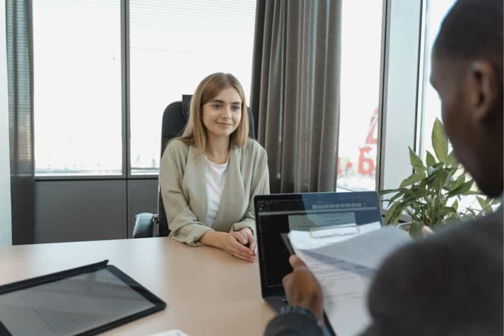 Woman smiling at a man in front of her during a job interview, both seated at a desk
