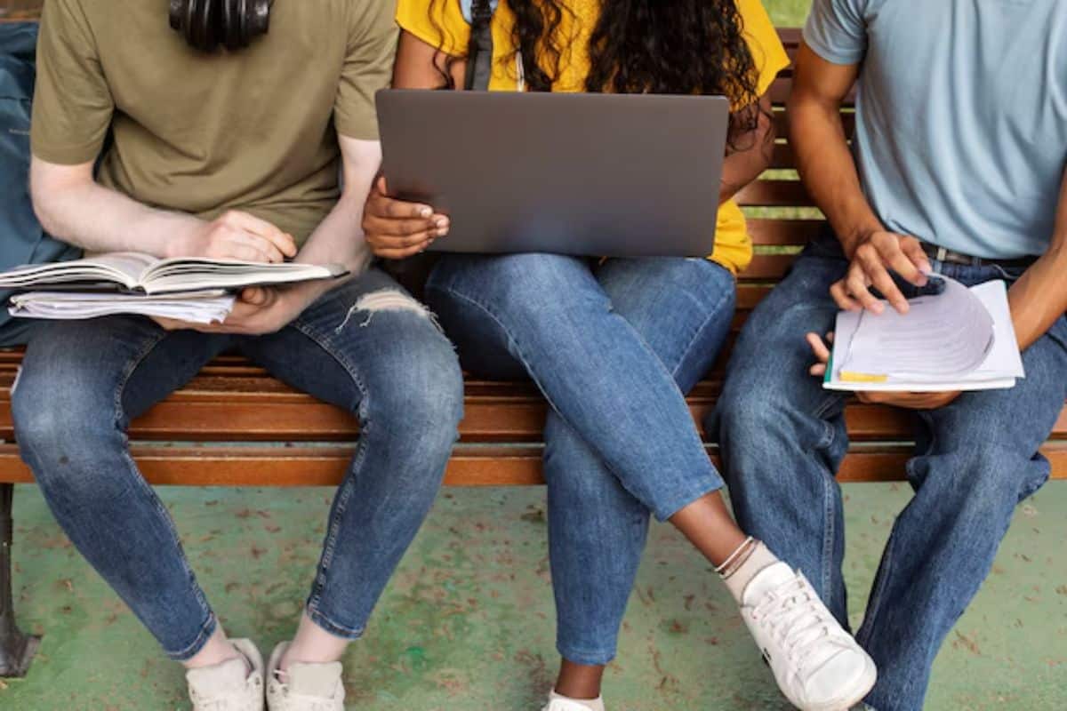 Drei Studenten sitzen auf einer Bank und arbeiten unabhängig voneinander an ihren Laptops und Papieren