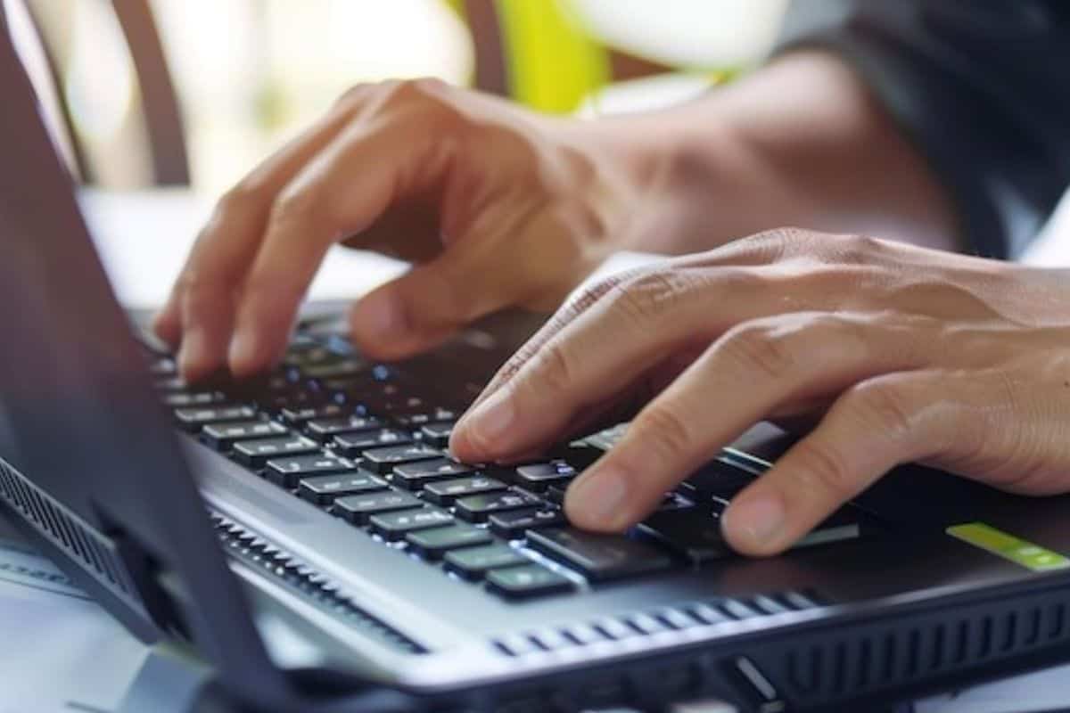 Close-up image of a man's hand typing on a laptop keyboard