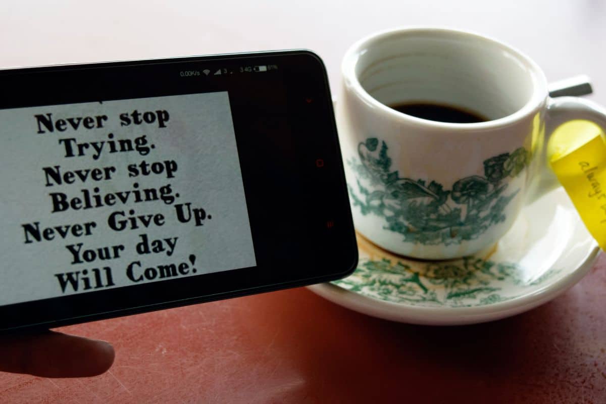 Cropped image of man holding phone with message by tea