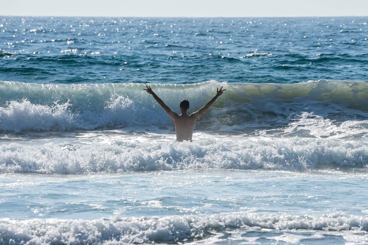 Carefree shirtless man with arms raised standing amidst sea