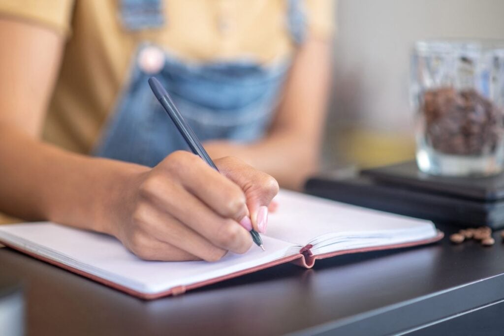 Womans thin graceful hand writing with pen in notebook 