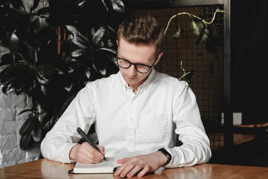 Man wearing sitting at table holding pen takes notes