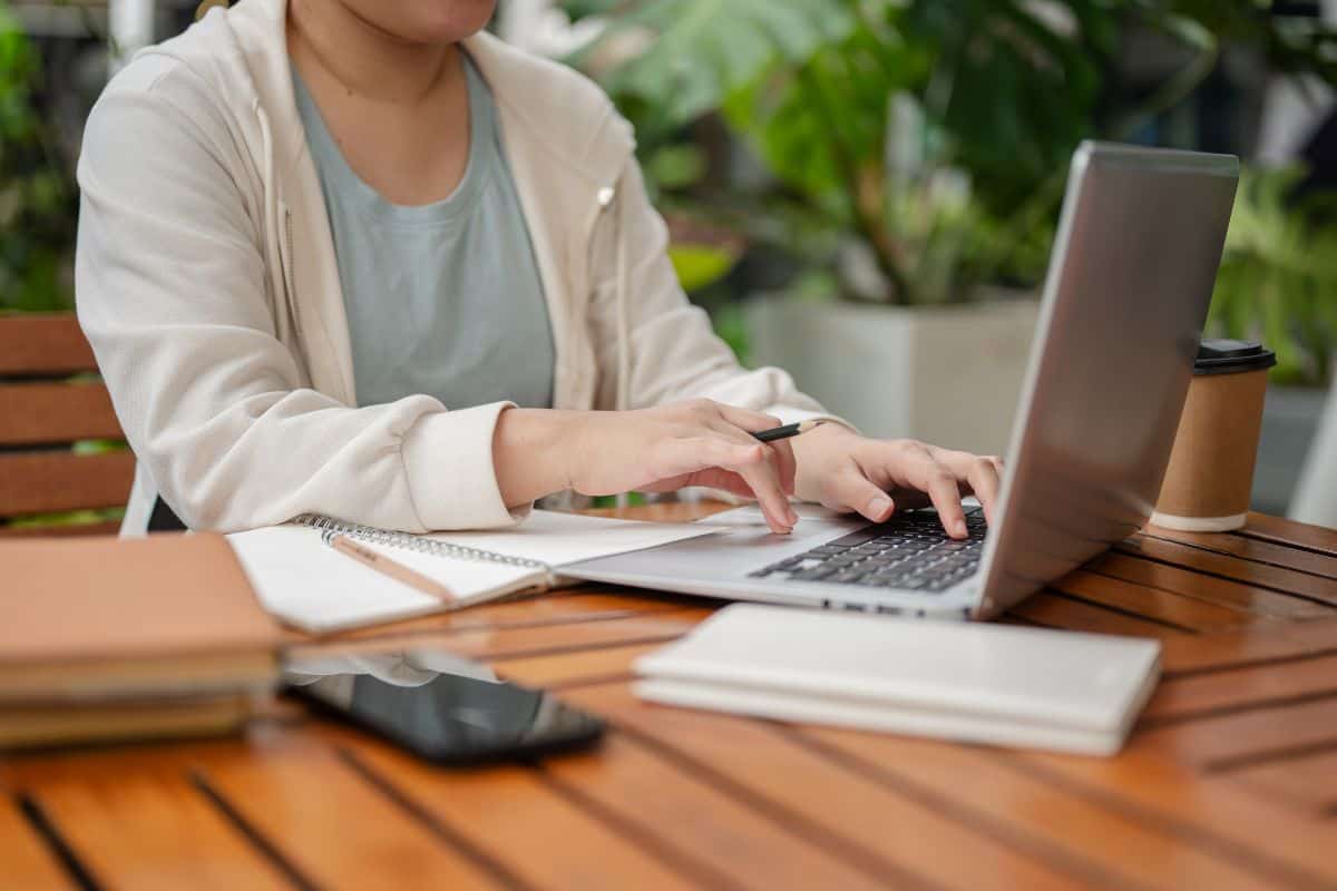 A woman is holding a pencil while typing on laptop