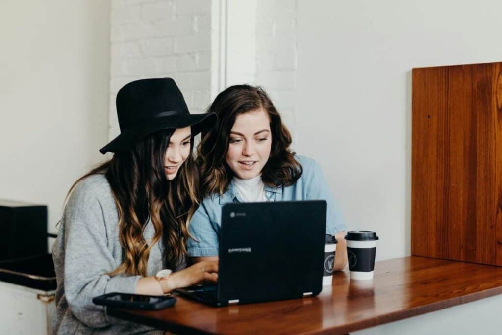 duas mulheres sentadas perto de uma mesa usando um laptop