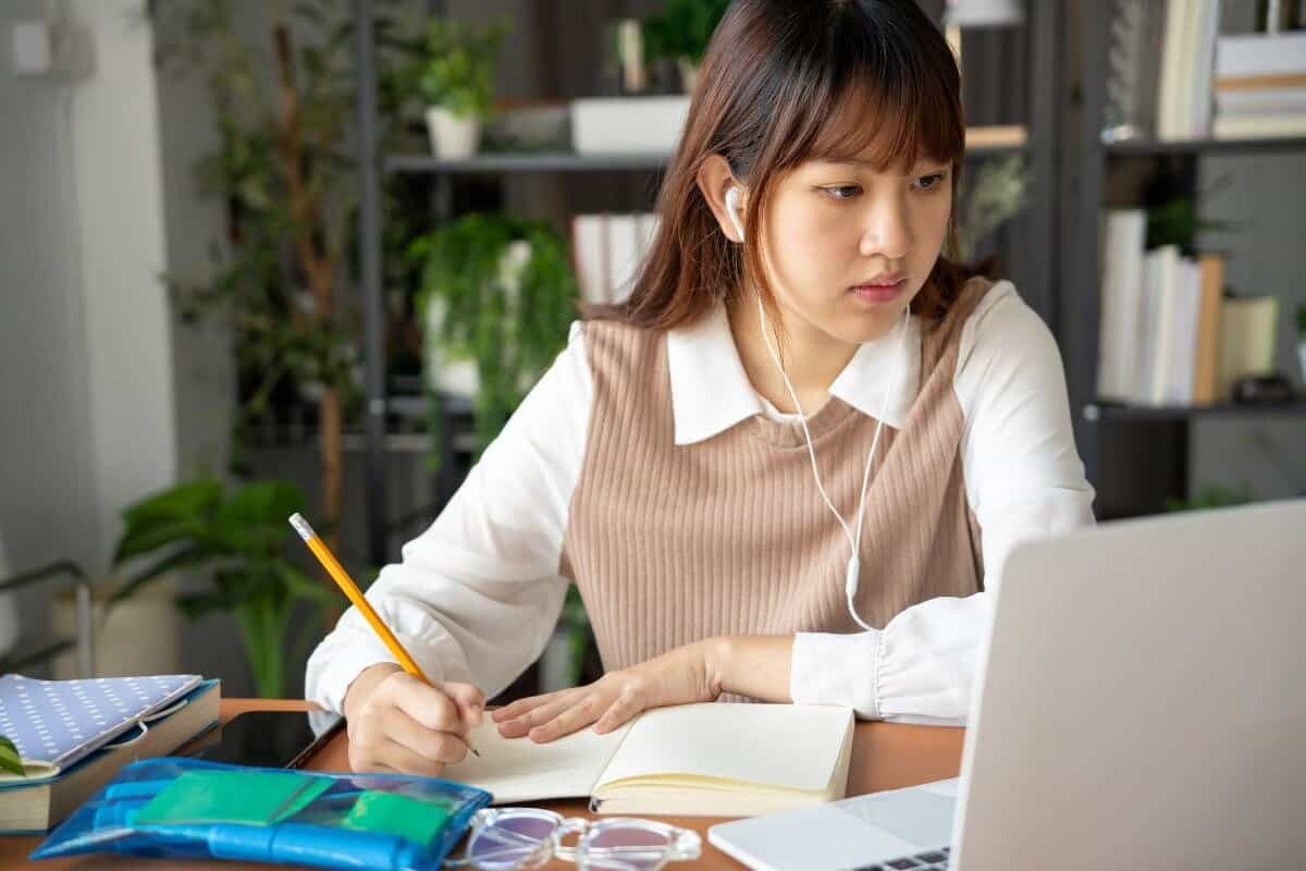 Estudiante trabajando con un cuaderno y un portátil sobre un escritorio