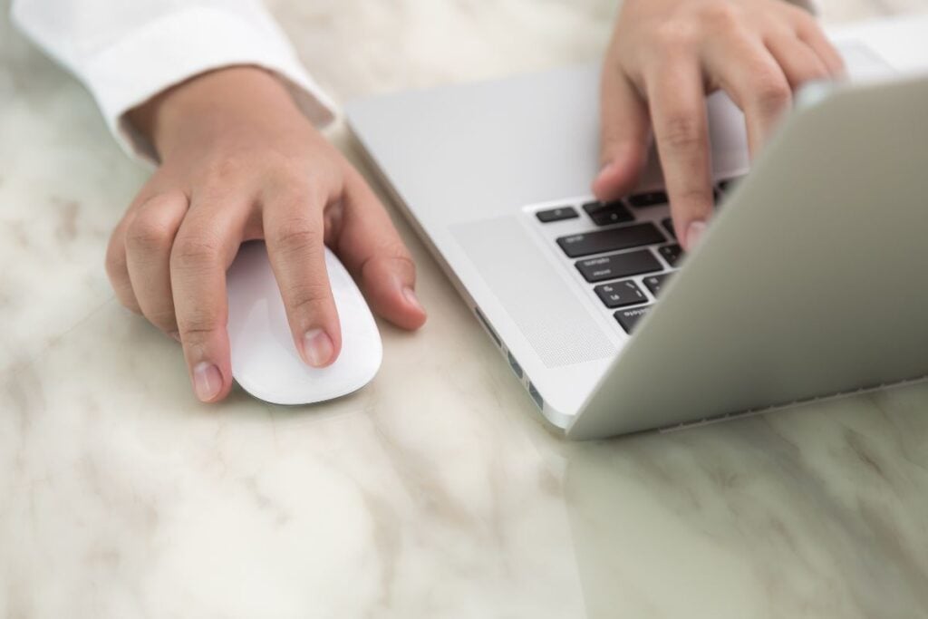 Person writing with one hand and the other touching a mouse