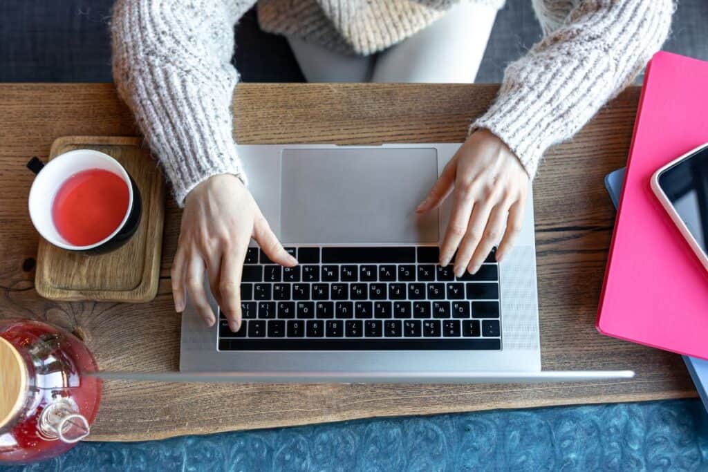 Woman working on a laptop in a cafe with a cup of tea top view