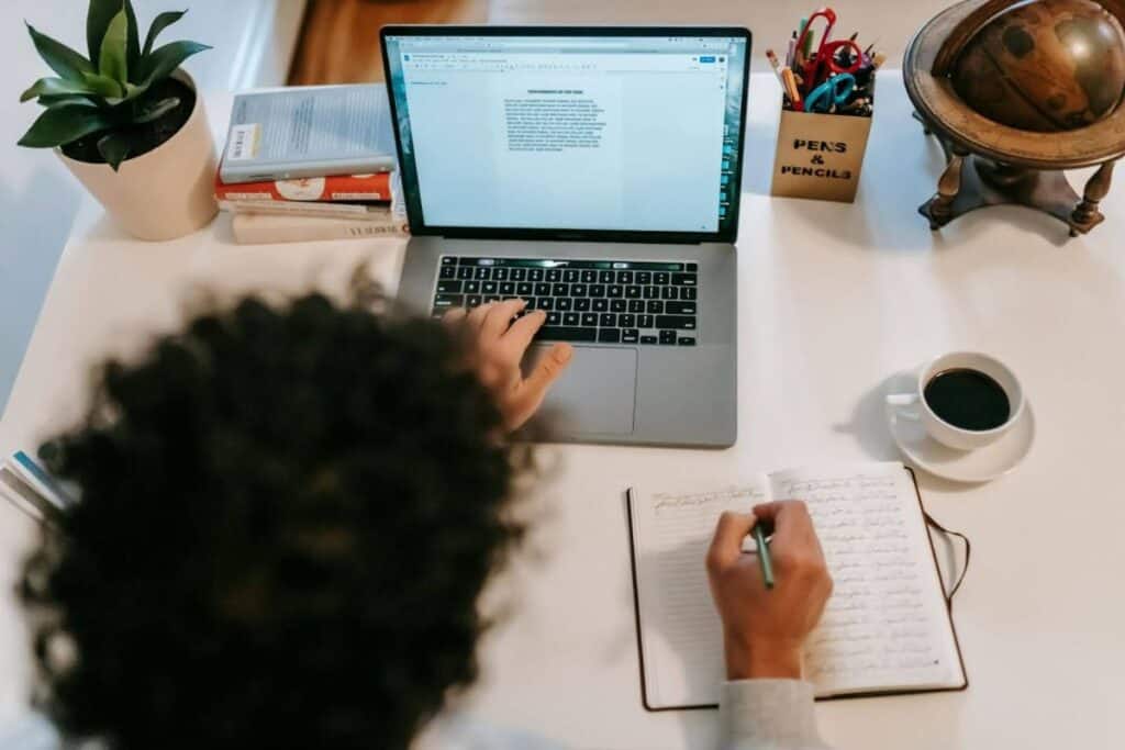 Unrecognizable author typing on laptop near coffee at home