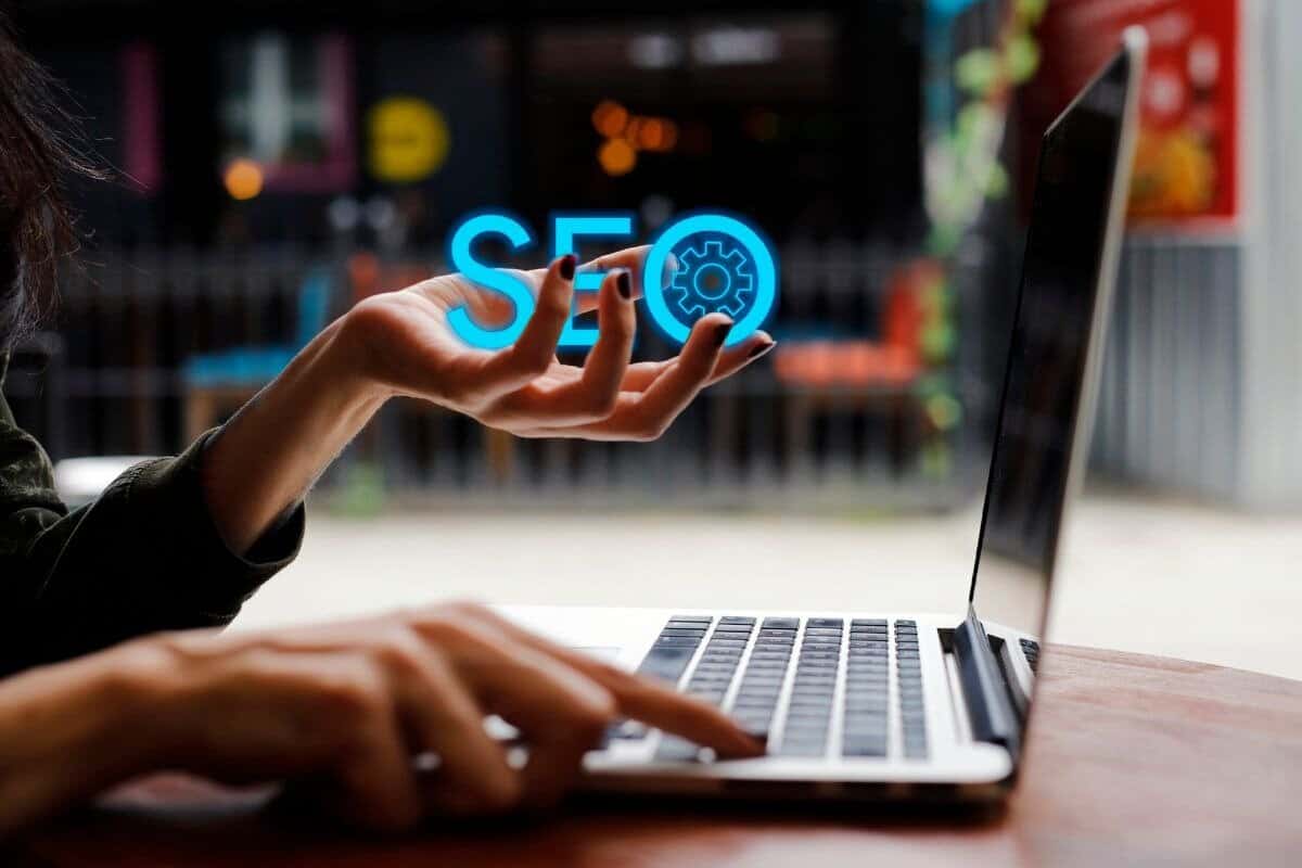 Woman typing on laptop while holding SEO text in other hand