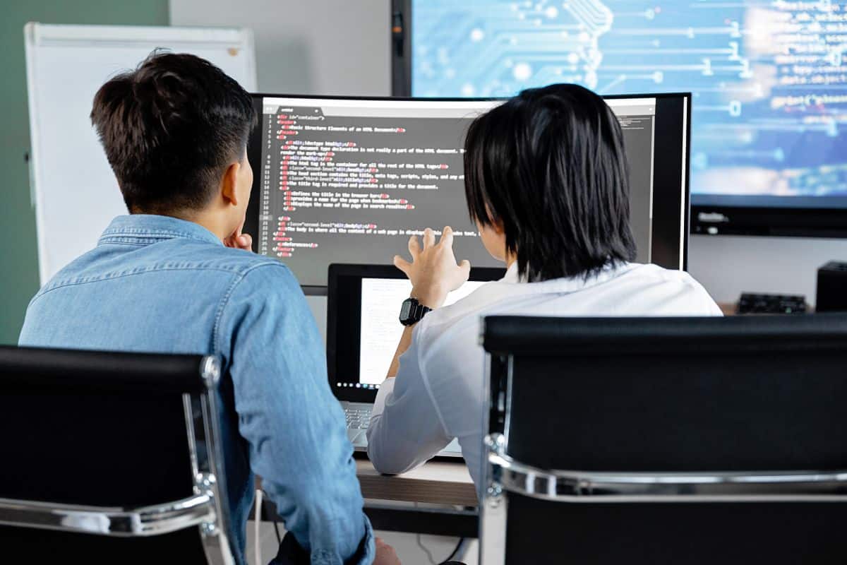 Duas pessoas colaborando na codificação em um computador, discutindo e revisando o código juntas.