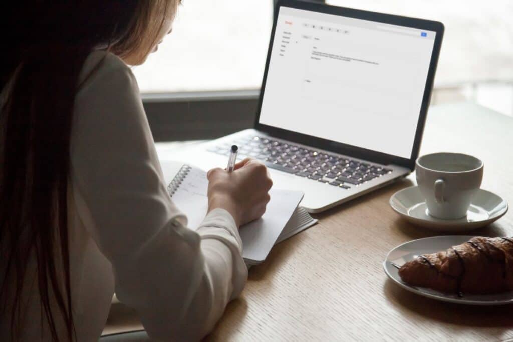 O que escrever em um e-mail ao enviar um currículo 7 Mulher fazendo anotações, lendo carta de e-mail em um laptop em um café