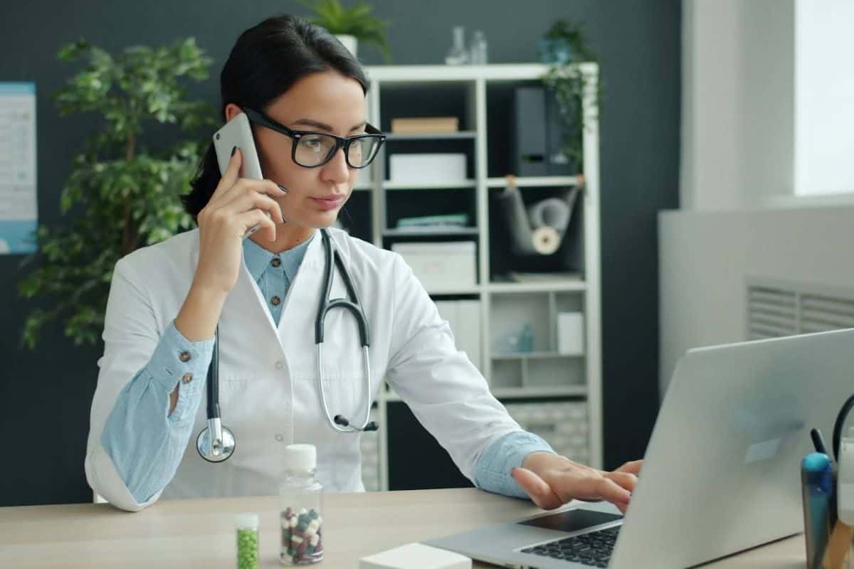 Doctor on phone, working on laptop in office.