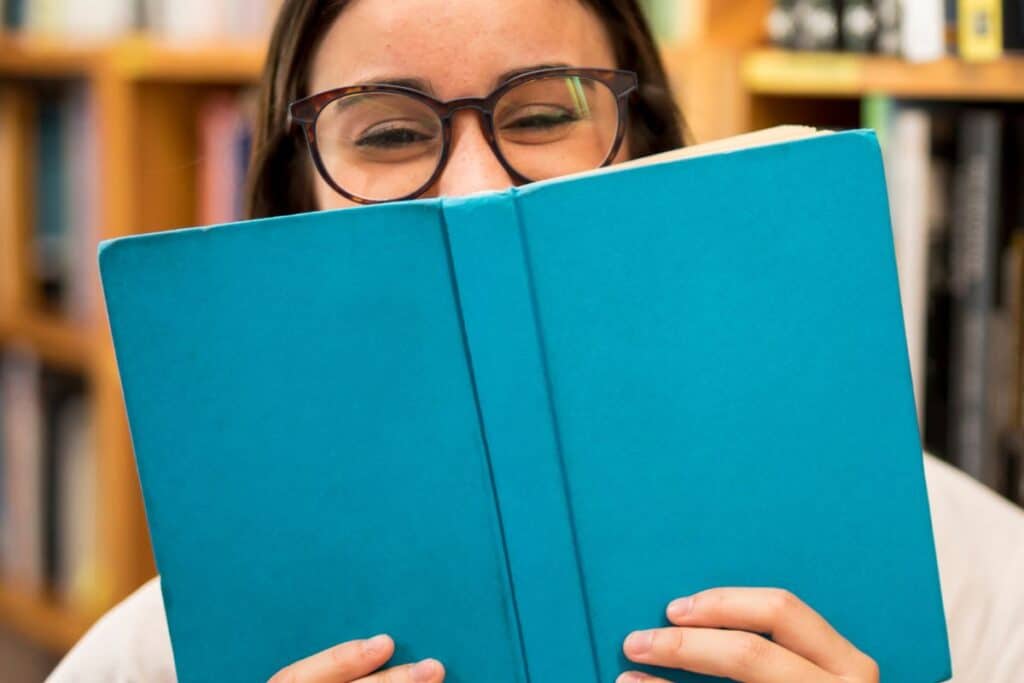 ¿Qué es un adagio? Definición y ejemplos claros 4 Adolescente risueña ocultando su rostro detrás de un libro
