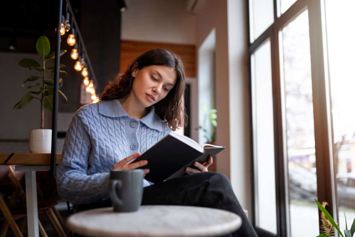 Persona en una cafetería leyendo un libro mientras toma un café.