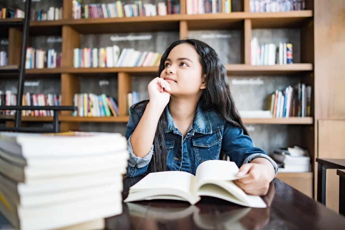 Young woman reading book sitting indoor in urban cafe