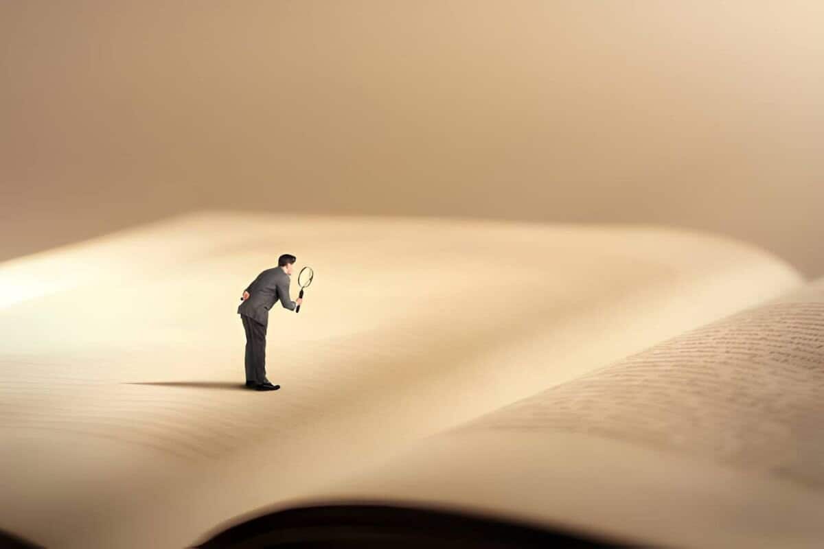Illustration d'une mini personne lisant un livre avec une loupe”
