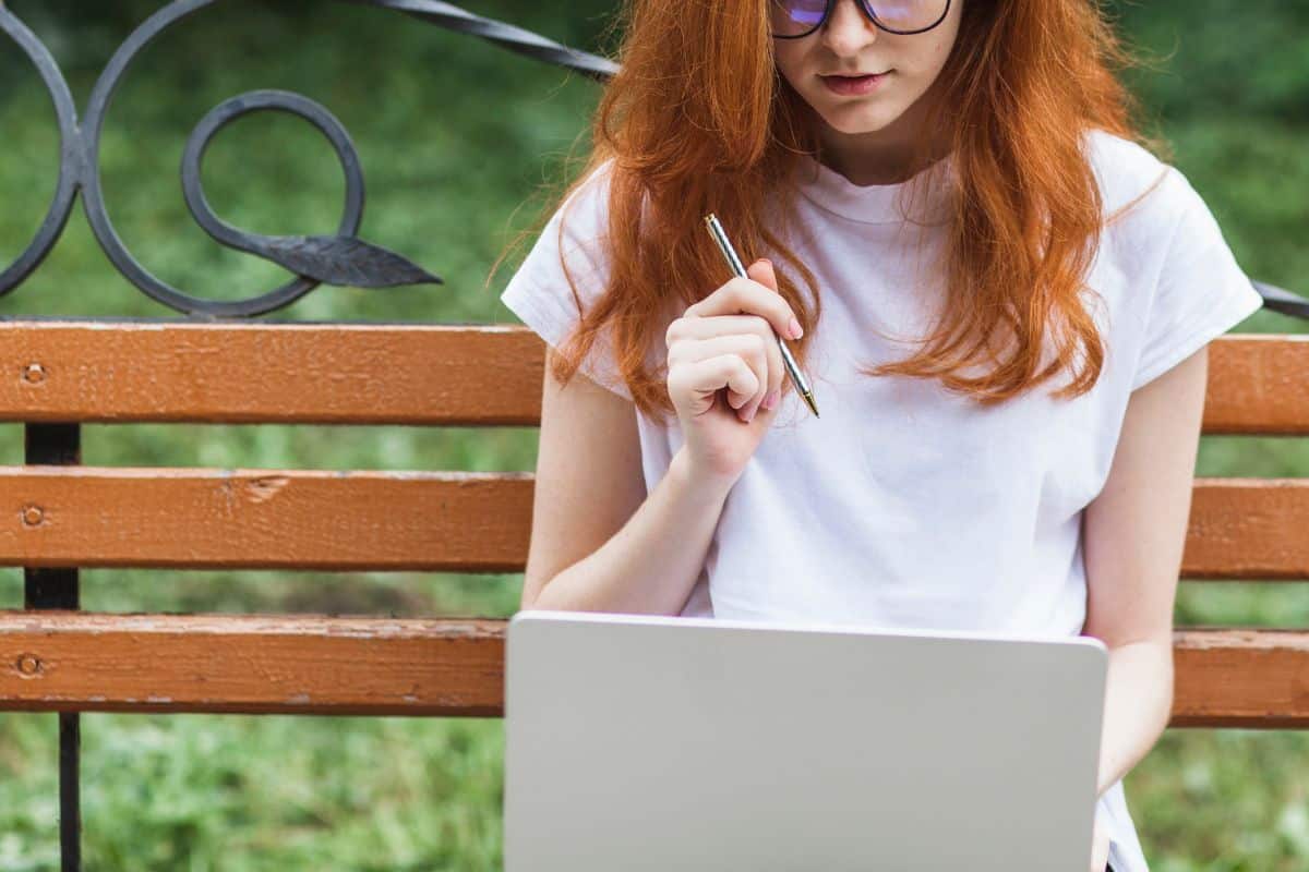 Woman sitting on bench with laptop and pen