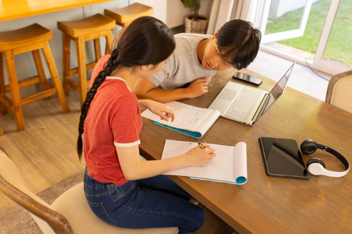 Studying together two students using laptop and notebooks table