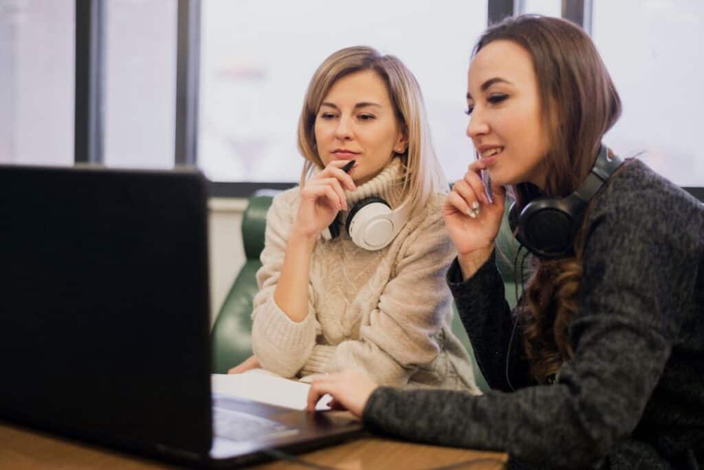 Mulheres usando fones de ouvido no pescoço e olhando para um laptop
