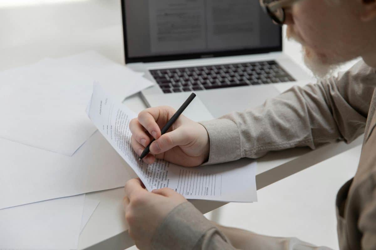 Crop office employee working with document near laptop